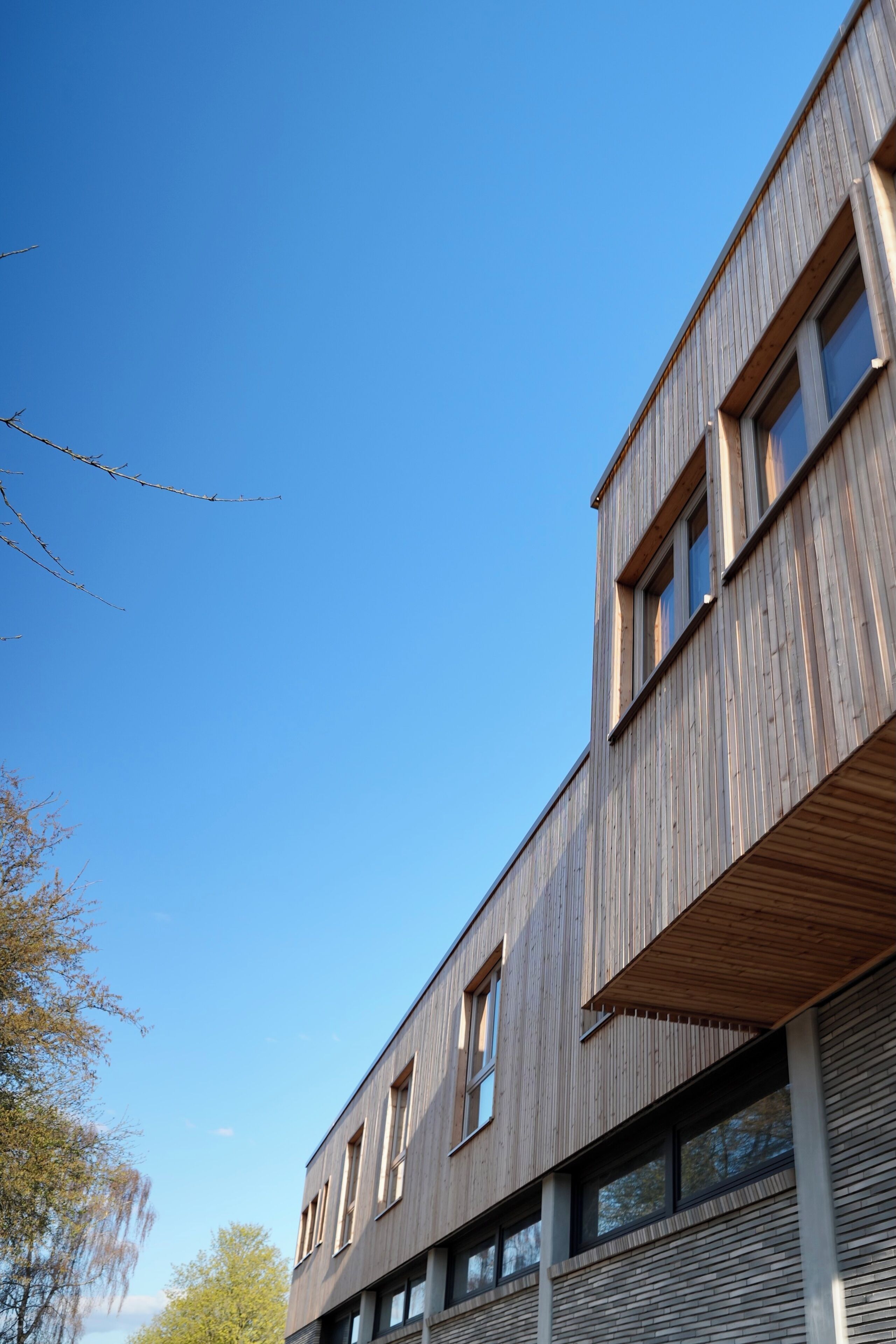 A modern building with a wooden facade, multiple windows, and a clear blue sky.