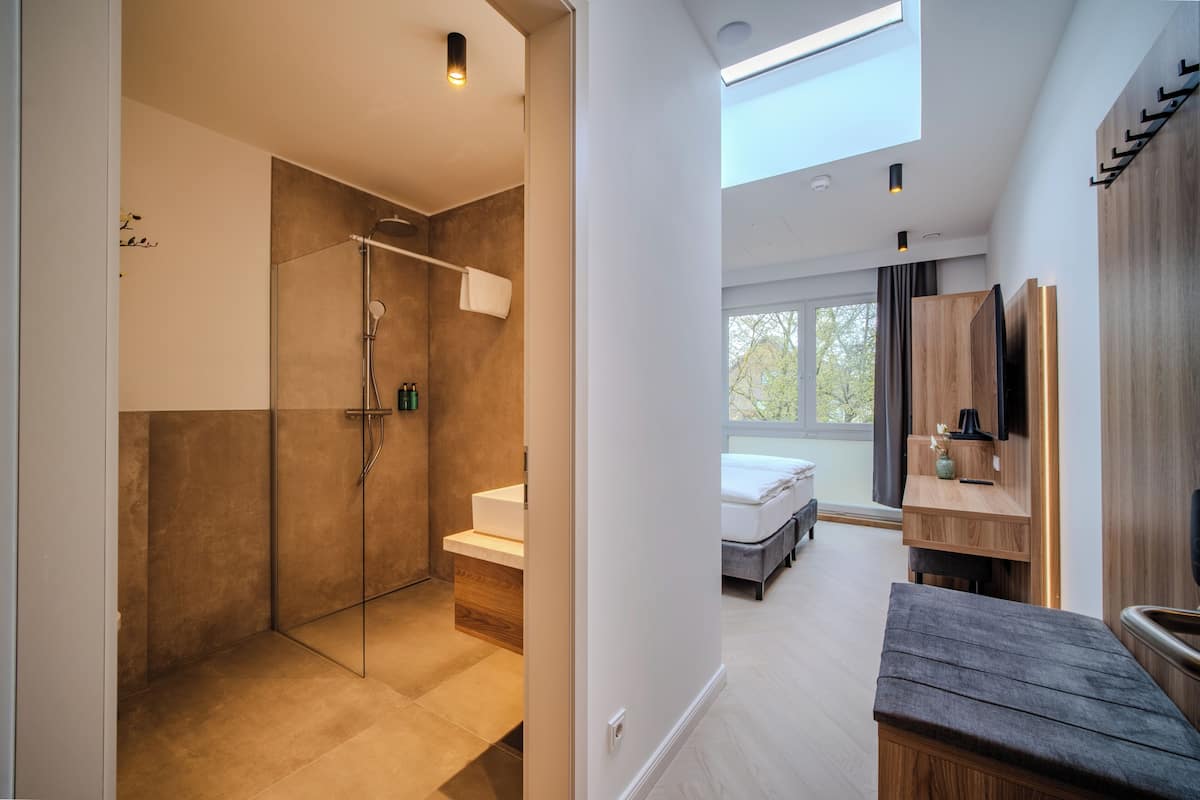 Un baño moderno con cabina de ducha de vidrio, un banco de madera y un espejo grande.