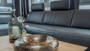 A modern living room with a leather sofa, a wooden coffee table, and a decorative glass vase with a candle. - MS Living Hotels (Langenhagen)