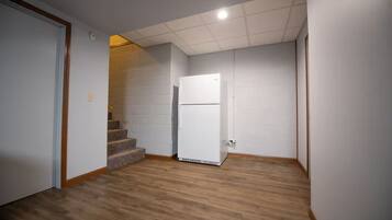 A room with a white refrigerator, a wooden floor, and a white brick wall.