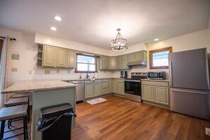 A kitchen with wooden flooring, a stainless steel refrigerator, a microwave, an oven, and light green cabinets.