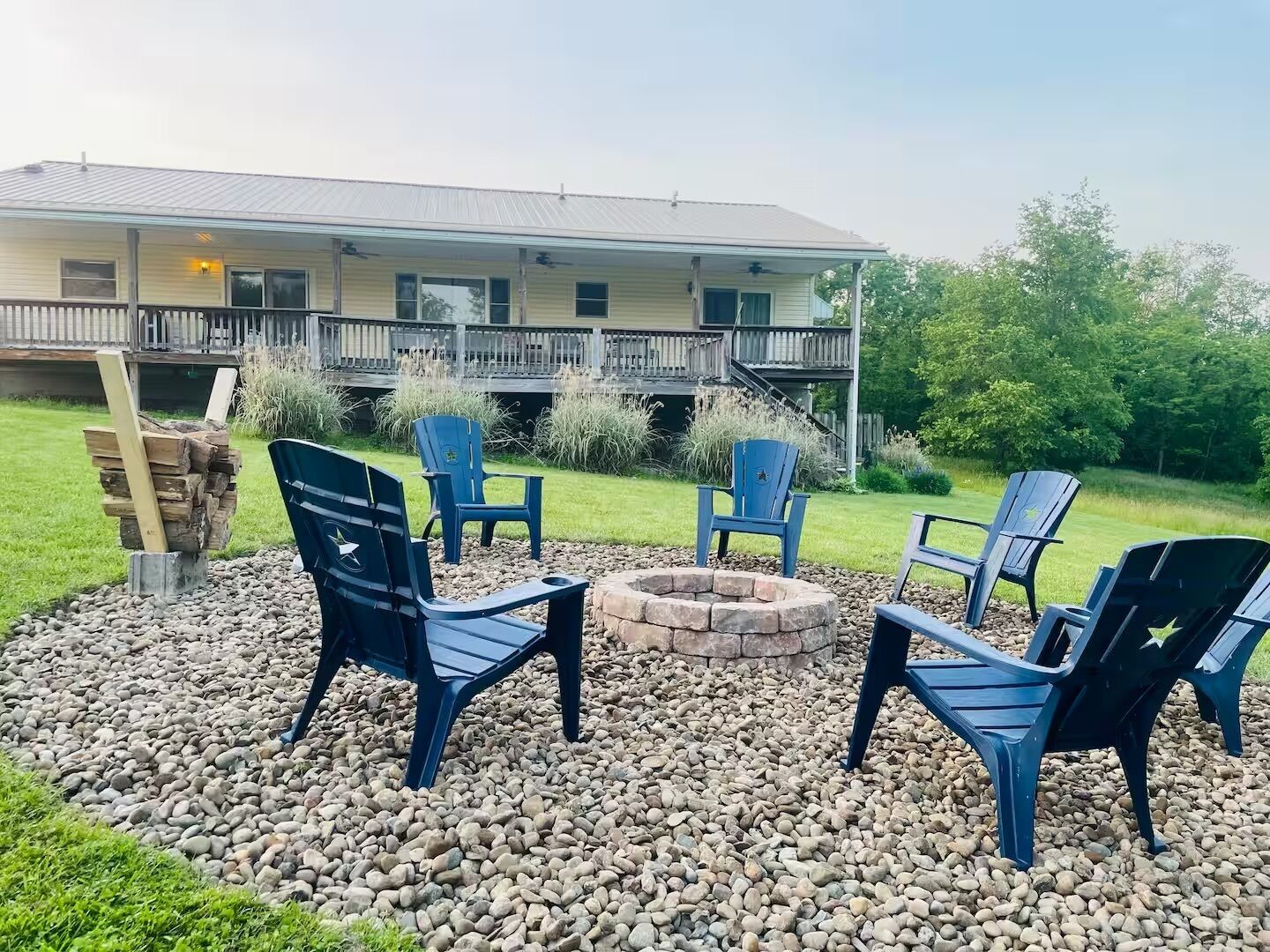 Une terrasse avec des fauteuils Adirondack, un foyer et une pile de bois de chauffage.