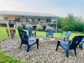 A patio with Adirondack chairs, a fire pit, and a stack of firewood.