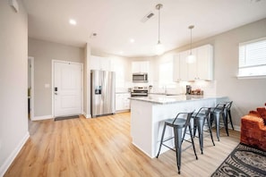 A modern kitchen with white cabinets, stainless steel appliances, and a central island with bar stools. - IRIE Living-Haven 2BR Home with Pool Gym Access (Whitestown)