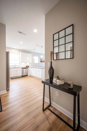 A modern kitchen with white cabinets, a black table with a vase, and a framed picture on the wall. - IRIE Living-Haven 2BR Home with Pool Gym Access (Whitestown)