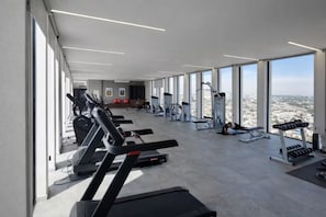 Ein Fitnessstudio mit Laufbändern, Kraftgeräten und Blick auf die Stadt.