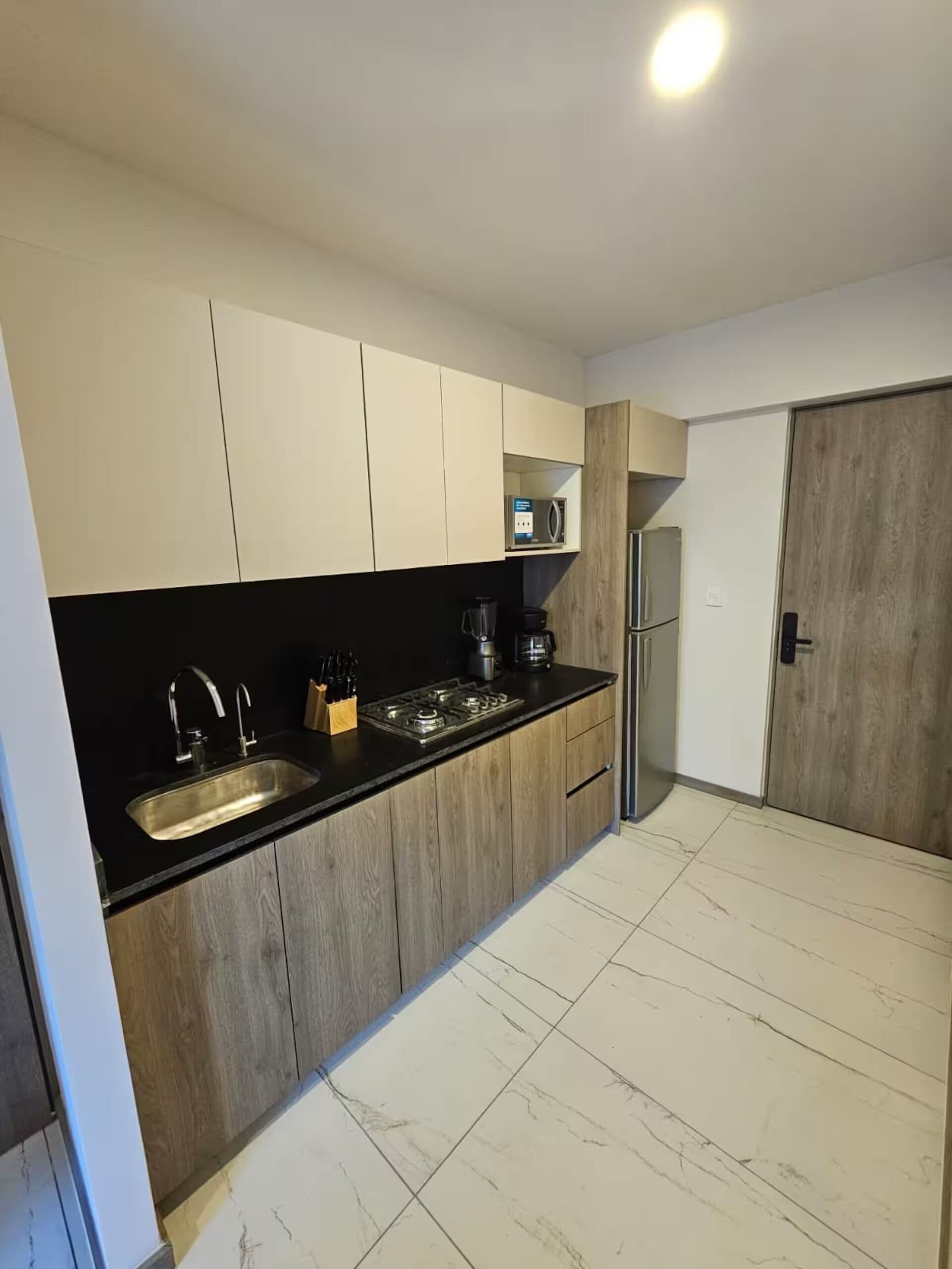 Una cocina moderna con encimera negra, pileta de acero inoxidable y muebles de madera.