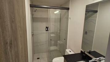 A modern bathroom with a glass-enclosed shower, a white toilet, and a black countertop with a sink and mirror.