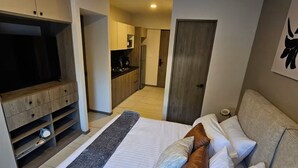 Ein Schlafzimmer mit Bett, Kissen, einem Fernseher, einer Küchenzeile und einer Tür zu einem weiteren Raum.