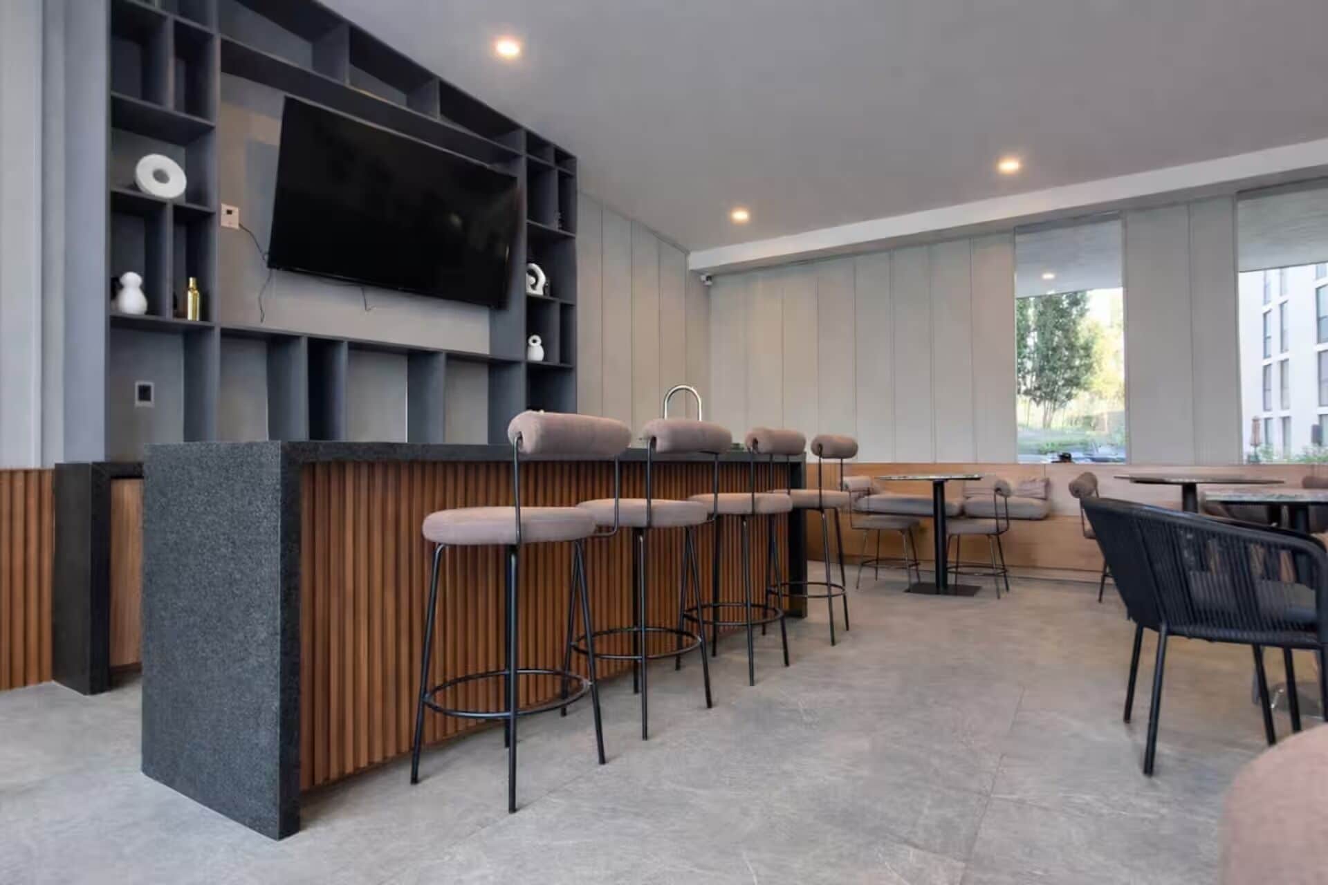 Una zona de bar moderna con una barra larga, varios taburetes y un televisor montado en la pared.