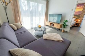A modern living room with a sofa, a coffee table, a TV, and a plant. - Stay. | T1 4-room 2-bathroom family garden apartment (Titisee-Neustadt)