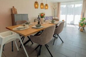 A dining area with a wooden table, chairs, and hanging pendant lights. - Stay. | T1 4-room 2-bathroom family garden apartment (Titisee-Neustadt)