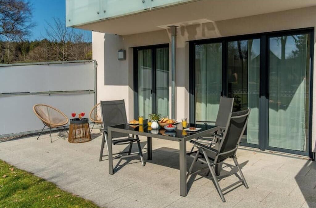 Un patio con un tavolo apparecchiato per due persone, circondato da sedie e vista su un edificio con ampie vetrate.