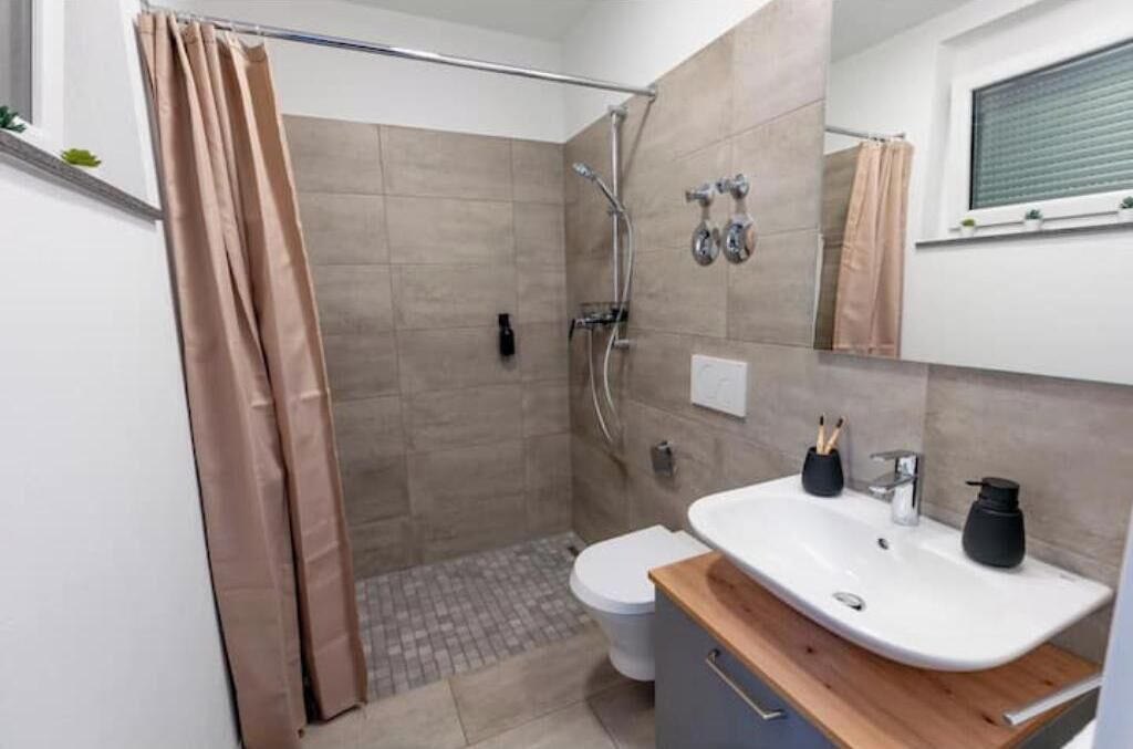 A bathroom with a shower, toilet, sink, and a mirror above the sink.