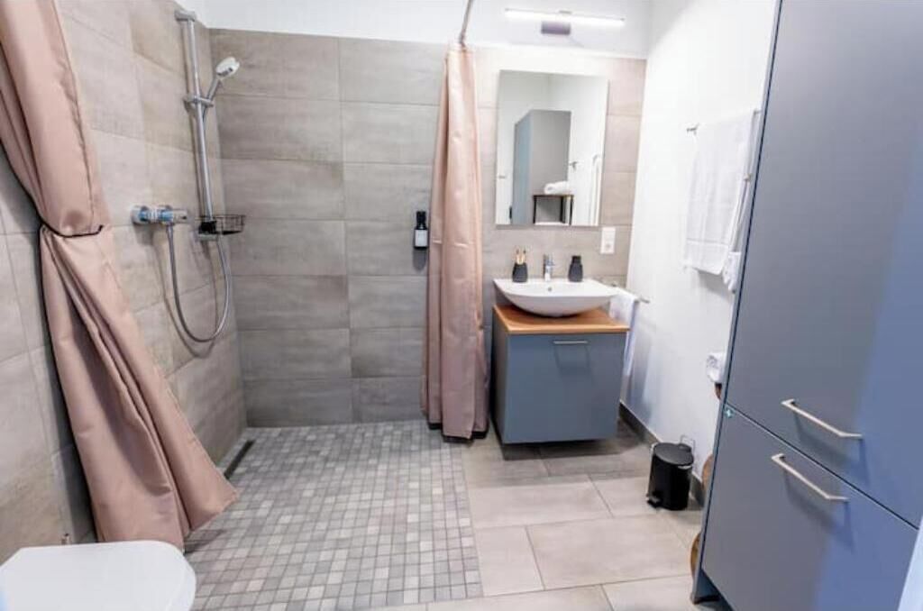 Een badkamer met douche, wastafel, spiegel en kastjes.