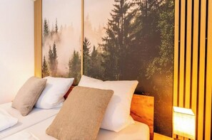 A hotel room with a bed, pillows, a wall-mounted lamp, and a forest-themed mural. - Stay. | T1 4-room 2-bathroom family garden apartment (Titisee-Neustadt)