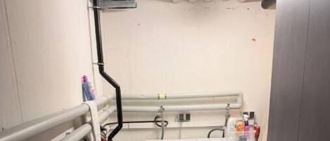 A laundry room with two front-loading washing machines, a small sink, and a trash bin.