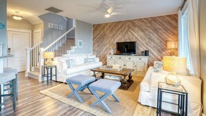 A living room with a sofa, coffee table, and TV, a staircase, and a herringbone-patterned wall.
