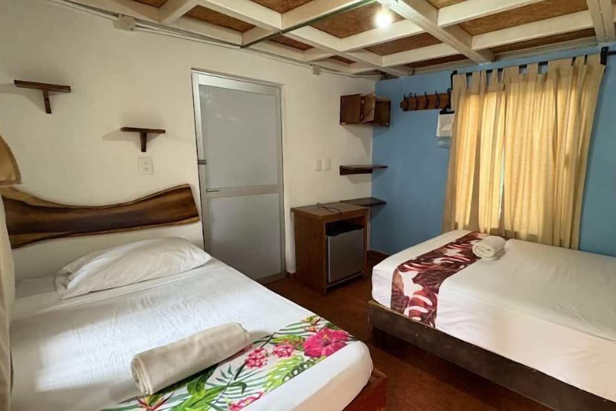 Una habitación con dos camas, un escritorio pequeño, un armario y una ventana con cortinas.