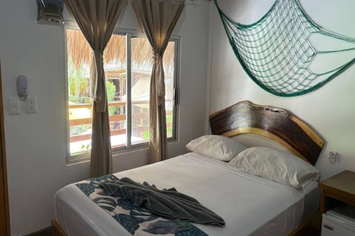 Una cama con cabecera de madera, una hamaca y una ventana con cortinas.