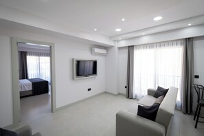 A modern hotel room with a bed, a sofa, a TV, and a balcony with curtains. - Ayayorgi Residence Cesme (Çeşme)