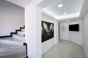 A modern interior with a staircase, a large wall art piece, a clock, and a flat-screen TV. - Ayayorgi Residence Cesme (Çeşme)