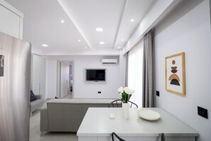 A modern kitchen with a dining area, white cabinetry, a flat-screen TV, and a vase with flowers on the table. - Ayayorgi Residence Cesme (Çeşme)