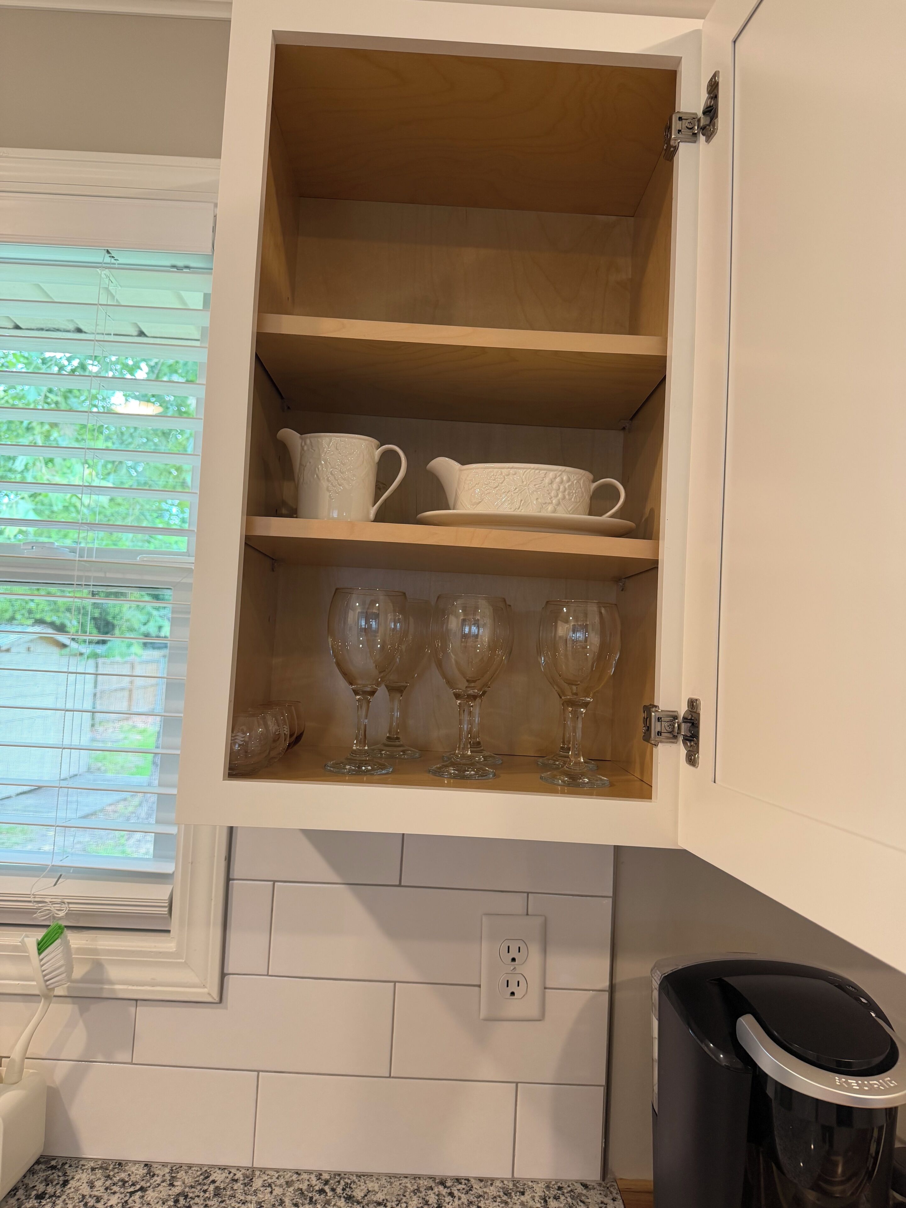 Una cocina con un armario que contiene vajilla de cerámica blanca y copas de vino.