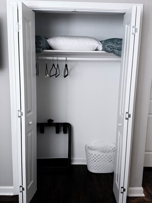 A walk-in closet with a hanging rod, a storage bench, and a laundry basket.