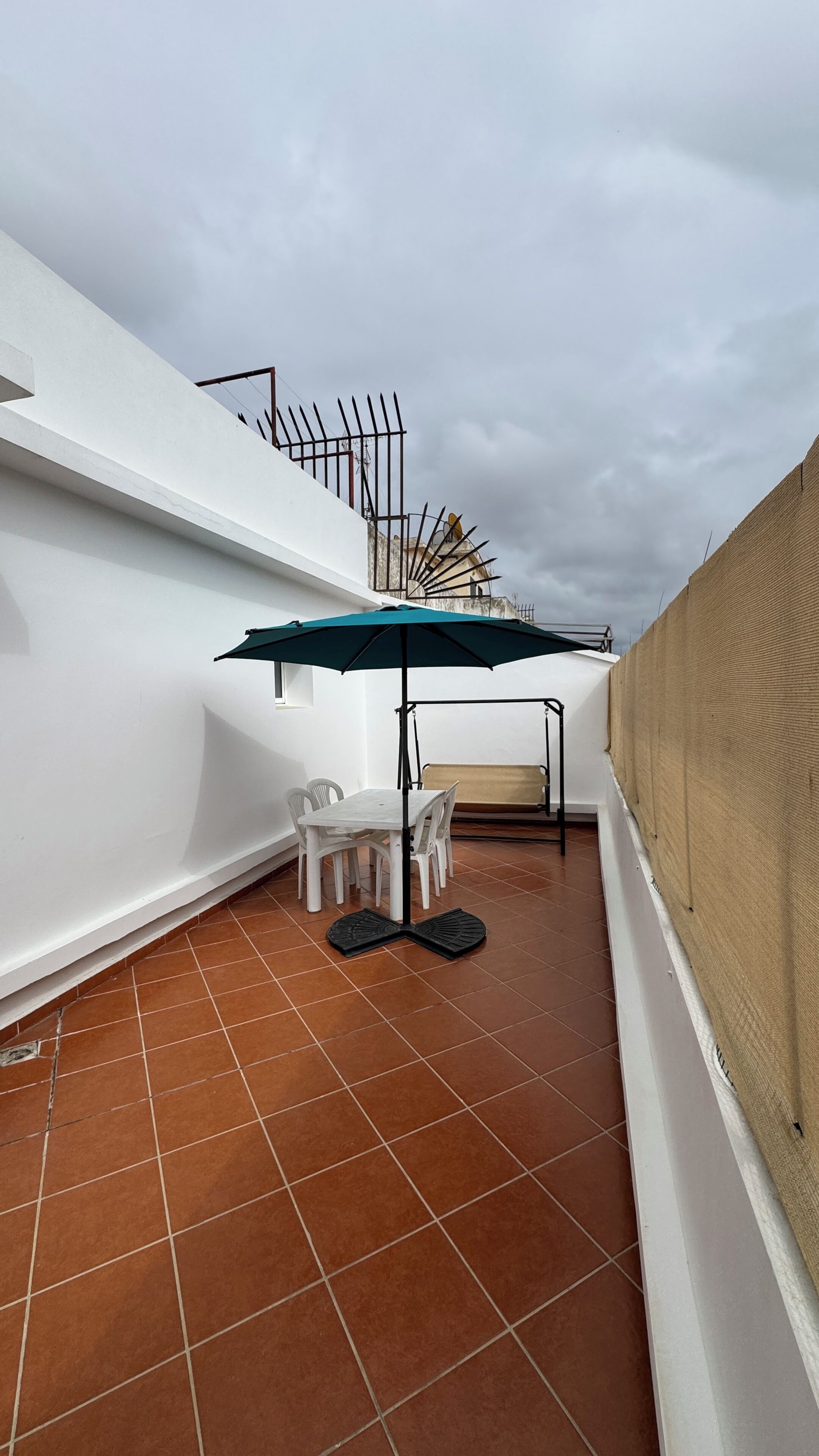 A terrace with a table and chairs, a swing, and a view of a building with a dome.