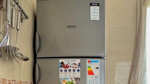 Een kleine keuken met een grijze koelkast, een gasfles en een set keukengerei aan de muur.