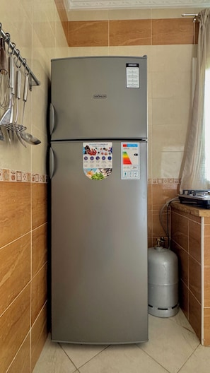 A compact kitchen with a grey refrigerator, a gas cylinder, and a set of kitchen utensils on the wall. - Apartment Sunny Terrace (Tanger)
