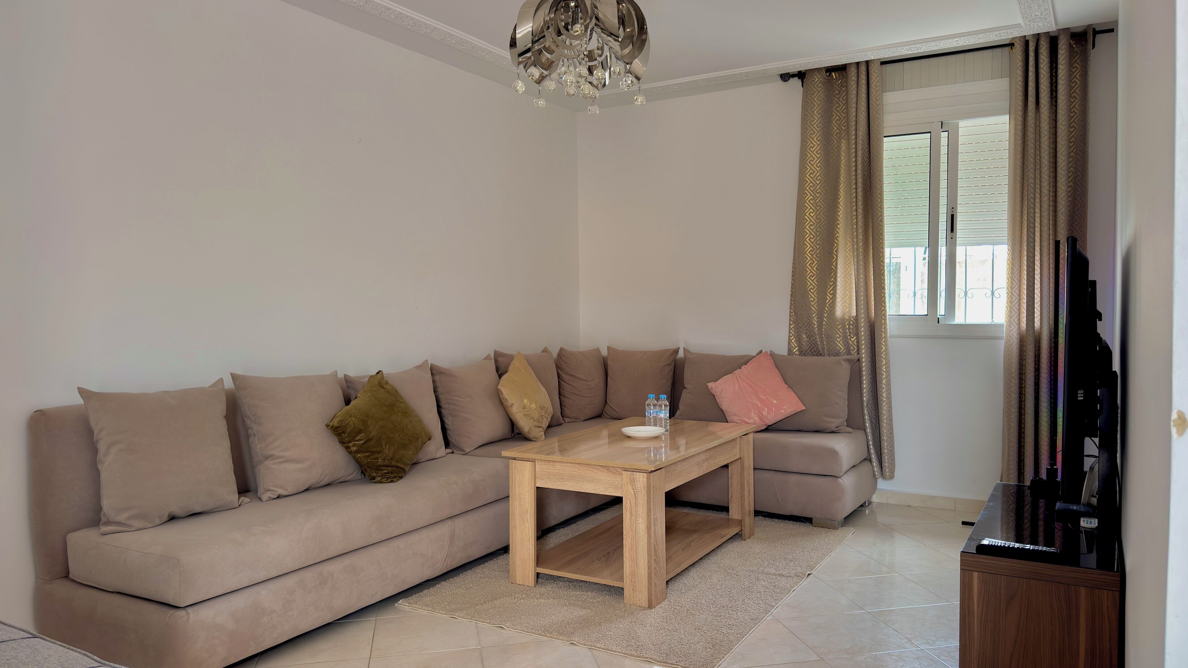 A living room with a beige sofa, a wooden coffee table, a television, and a window with curtains.