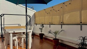 Een terras met een tafel, stoelen, plantenpotten en een grote parasol.