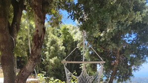 Una silla hamaca con un cojín azul, sillas blancas y vistas al paisaje.