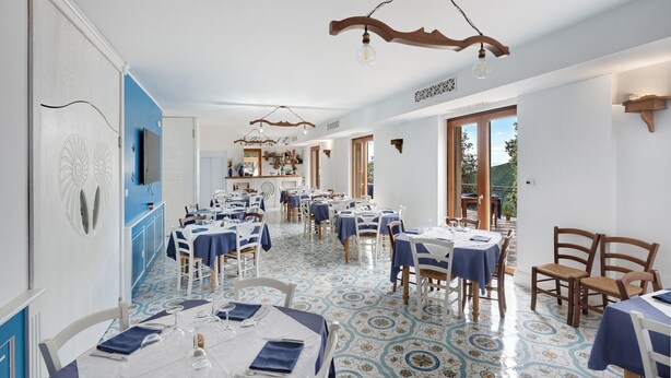 Un restaurante con mesas preparadas para comer, una zona de cocina y una vista a través de la puerta abierta.