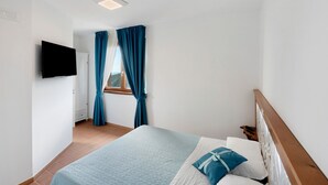 Un dormitorio con cama, televisor montado en la pared, ventana con cortinas y cabecera de madera.