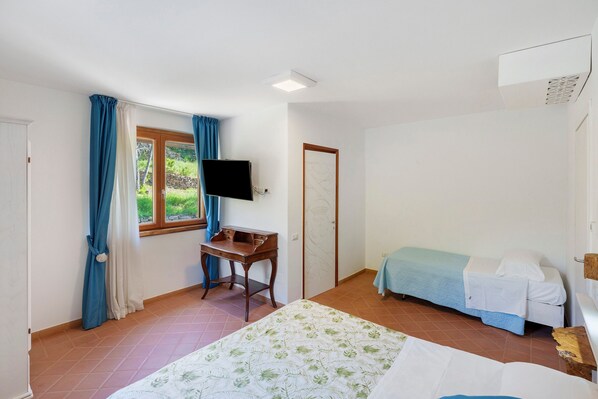 A bedroom with a bed, a desk, a television, and a window with curtains.