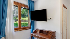 Et værelse med et træskrivebord, et ophængt fjernsyn, et vindue med blå gardiner og en dør med dekorativt panel.