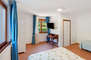 Un dormitori amb llit, escriptori, televisió i finestra amb cortines.