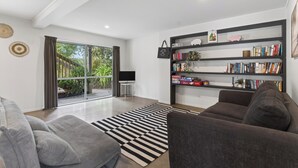 Un salon moderne avec un canapé gris, un tapis noir et blanc, une bibliothèque et une grande fenêtre avec des rideaux.