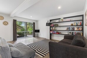 Ein modernes Wohnzimmer mit einem grauen Sofa, einem schwarz-weißen Teppich, einem Bücherregal und einem großen Fenster mit Vorhängen.