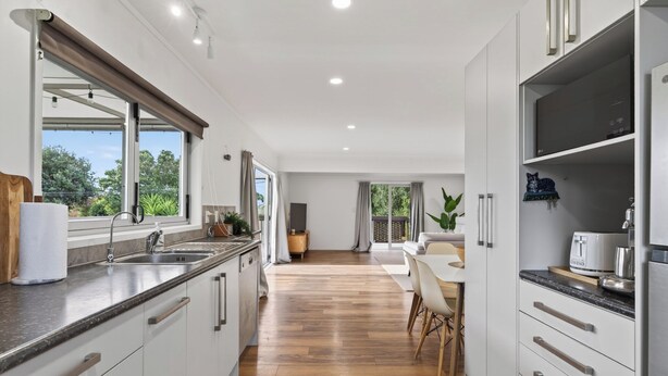 Une cuisine moderne avec un plancher en bois, des meubles blancs et une grande fenêtre.