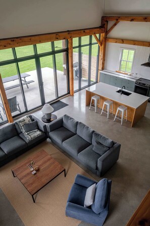 A modern interior with a large window, a kitchen island, and a seating area. - Black Ridge Barn - Minimalist Restored Barn (Prince Edward County)
