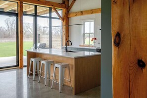 A kitchen with a large island, wooden beams, and large windows. - Black Ridge Barn - Minimalist Restored Barn (Prince Edward County)