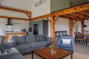 A modern living room with a grey sofa, a wooden coffee table, and a dining area with wooden chairs. - Black Ridge Barn - Minimalist Restored Barn (Prince Edward County)