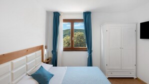A bedroom with a bed, a wardrobe, a window with curtains, and a view of greenery outside. - Zenone Room with Sea View, Wi-Fi and Air Conditioning (Serramezzana)