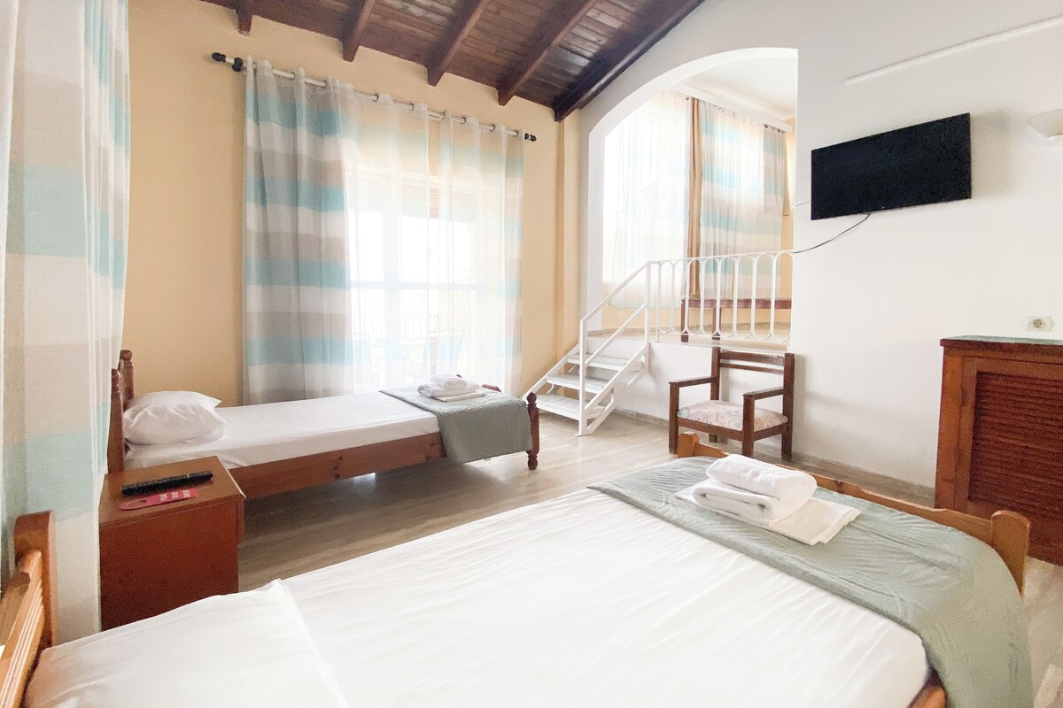 A bedroom with a bed, a chair, a small table, a nightstand, a TV, and a staircase.