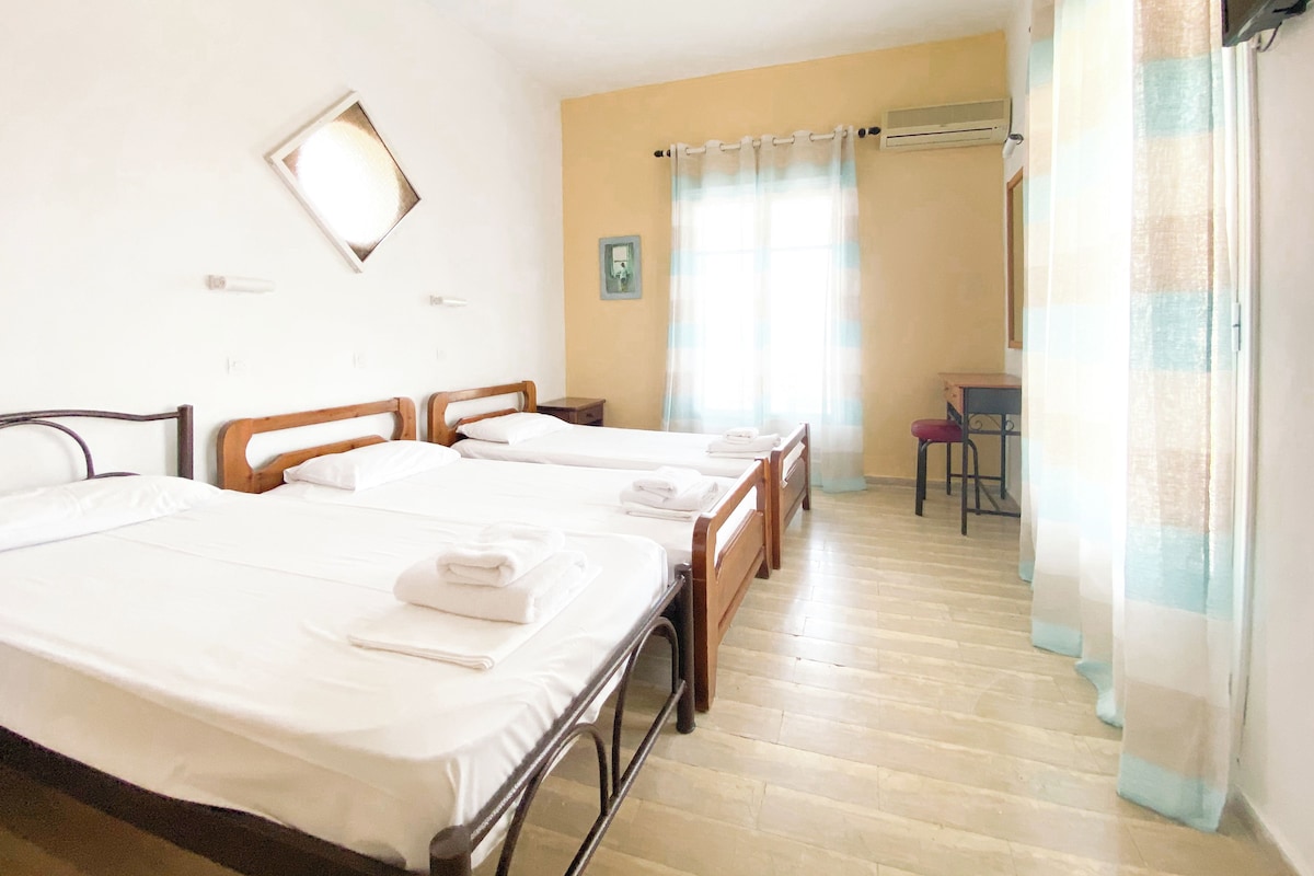 A hotel room with three beds, a desk, a chair, and a window with curtains.