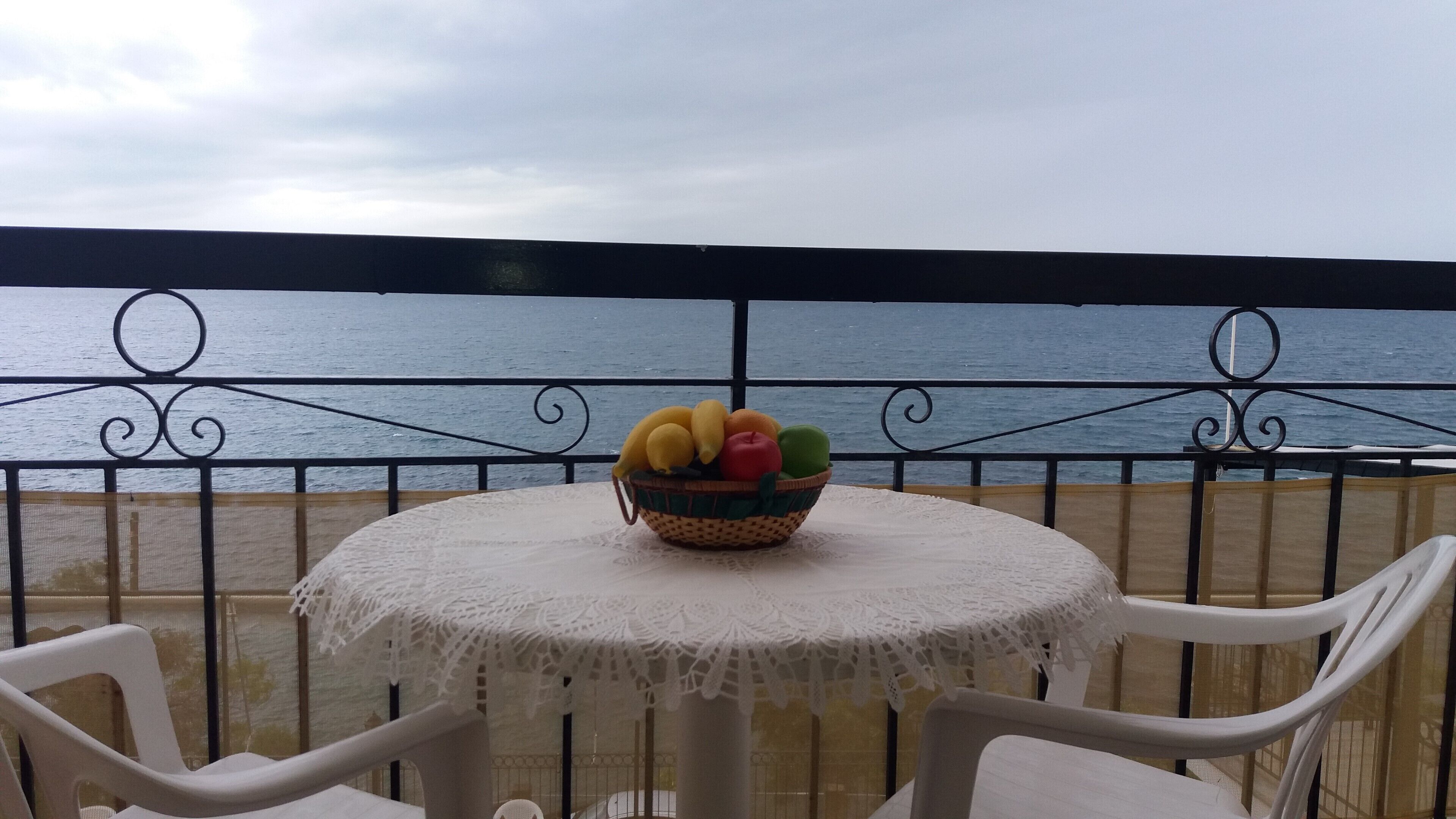 A table with a fruit basket on a balcony with a view of the sea.